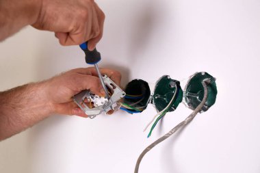 Bir işçi tornavida kullanarak duvara elektrik prizi takıyor..