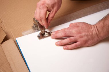 Erkeklerin elleri dolap kapısına bir mobilya menteşesi yerleştirir. Kapıya bir mobilya menteşesi takmak. Mobilya montajı ve montajı. 