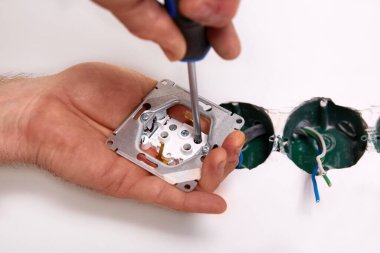 Elektrikçi tornavida kullanarak duvara elektrik prizi takıyor..