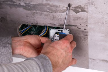 Elektrikçi porselen fayanslardan yapılmış bir duvara elektrik prizleri yerleştiriyor. Ev elektriği tamiri devam ediyor. Duvardaki aletler ve kablolarla birlikte..