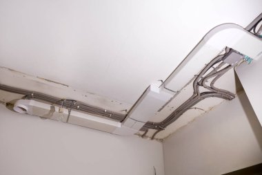 Tavana elektrik tesisatı ve havalandırma kurulumu. Koruyucu bir borunun elektrik kabloları, odanın tavanında havalandırma kutuları yenileniyor..