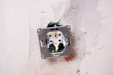 Duvara monte edilen bir elektrik prizinin yakın çekim görüntüsü. Arka plan kısmen korunmasız bir duvar gösteriyor, bu da yenileme çalışmalarını gösteriyor.. 