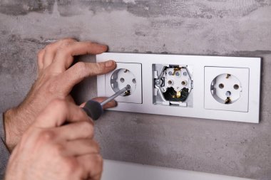 Adamın biri porselen bir duvara elektrik prizi takmak için tornavida kullanıyor..