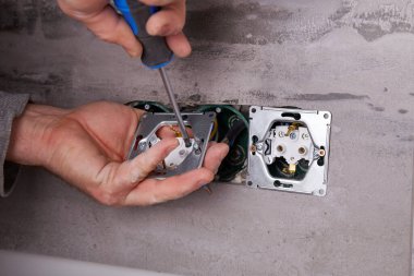 Elektrikçi porselen fayanslardan yapılmış bir duvara elektrik prizleri yerleştiriyor. Ev elektriği tamiri devam ediyor. Duvardaki aletler ve kablolarla birlikte..
