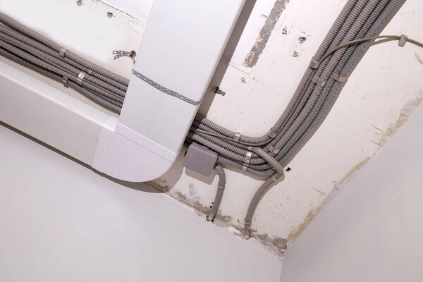 Installation of electrical wiring and ventilation on the ceiling. Electrical wiring in a protective corrugated pipe, ventilation boxes on the ceiling in the room being renovated.
