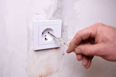 Elektrikçi gösterge tornavidayla prizdeki voltajı kontrol ediyor. Odada elektrik tesisatı ve onarım çalışmaları yapılıyor.. 