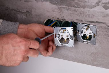 Bir işçi tornavida kullanarak duvara elektrik prizi takıyor..