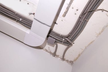 Tavana elektrik tesisatı ve havalandırma kurulumu. Koruyucu bir borunun elektrik kabloları, odanın tavanında havalandırma kutuları yenileniyor..