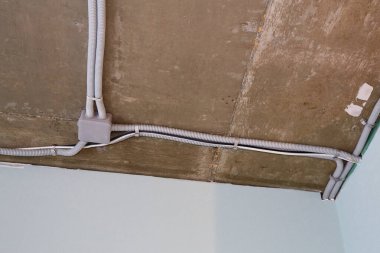 Koruyucu kablo tüpündeki elektrik kabloları ve bağlantı kutusu düzgünce tavana yerleştirilmiş. Tamir odasına elektrik tesisatı kurulumu.