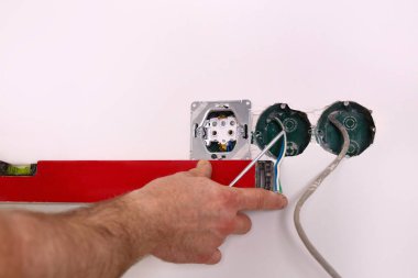  Bir elektrikçi prizlerin seviyesini kontrol etmek için bina seviyesini kullanır. Elektrik prizlerinin kurulumu üzerinde çalış.