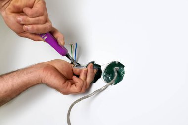 Yetenekli elektrikçi, bıçak aletini hassasiyet için kullanarak duvardaki elektrik kablolarını dikkatlice bağlar. Görevde güvenlik ve ayrıntılara dikkat edilmesi açıkça görülüyor.. 