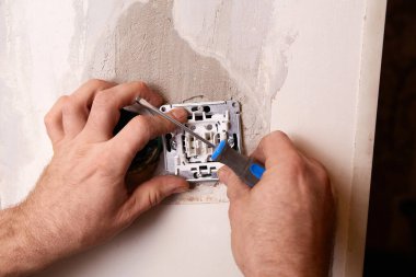 Elektrikçi beyaz bir duvara elektrik prizi takmak için tornavida kullanır. Kapalı alanda yenileme çalışması