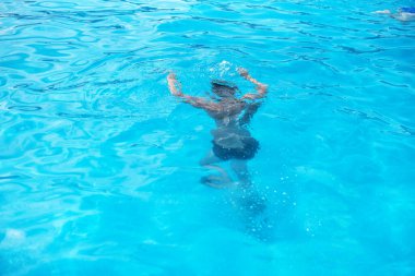 Güneşli bir günde yüzme havuzunda gözlüklü bir çocuk. Çocuklar Yaz Eğlencesi. Yaz tatilinde çocuklar su sporu yapıyor..