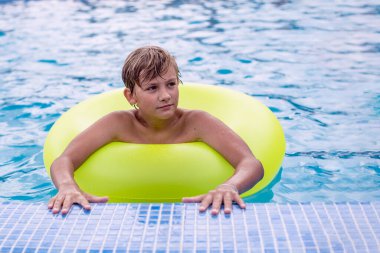 Yüzme havuzunda dinlenen şişme yüzüklü genç bir çocuk. Çocuklar yaz eğlencesi, tatil, güneşli bir gün. Yaz tatilinde çocuklar su sporu yapıyor..