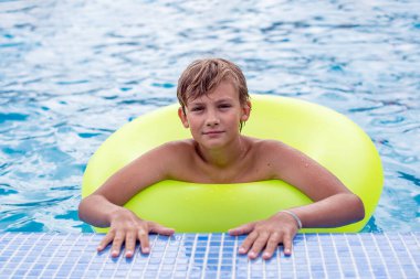 Yüzme havuzunda dinlenen şişme yüzüklü genç bir çocuk. Çocuklar yaz eğlencesi, tatil, güneşli bir gün. Yaz tatilinde çocuklar su sporu yapıyor..