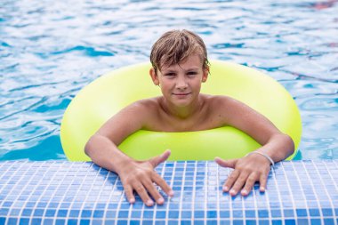 Yüzme havuzunda dinlenen şişme yüzüklü genç bir çocuk. Çocuklar yaz eğlencesi, tatil, güneşli bir gün. Yaz tatilinde çocuklar su sporu yapıyor..