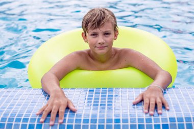 Yüzme havuzunda dinlenen şişme yüzüklü genç bir çocuk. Çocuklar yaz eğlencesi, tatil, güneşli bir gün. Yaz tatilinde çocuklar su sporu yapıyor..