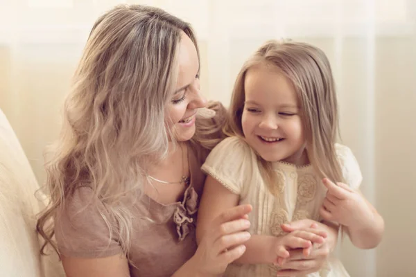 Smiling preschool girl sitting on mommies lap at home. Carefree mom and little girl laughing while playing at home. Love, warm family relationships. Happy kid with mum spending free time together.