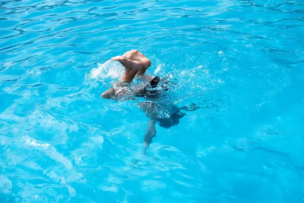 Güneşli bir günde yüzme havuzunda gözlüklü bir çocuk. Çocuklar Yaz Eğlencesi. Yaz tatilinde çocuklar su sporu yapıyor..