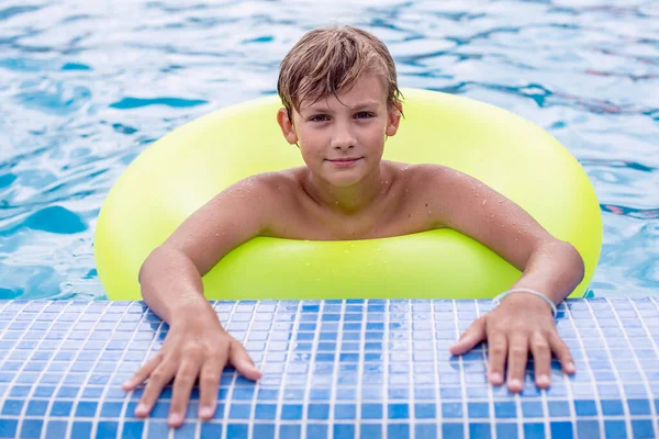 Yüzme havuzunda dinlenen şişme yüzüklü genç bir çocuk. Çocuklar yaz eğlencesi, tatil, güneşli bir gün. Yaz tatilinde çocuklar su sporu yapıyor..