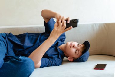 Ergen çocuk evinde koltukta oturup arkadaşlarıyla mesajlaşarak, internetten alışveriş yaparak ya da mobil uygulama ya da sosyal medyayı kontrol ederek rahatlıyor. Akıllı telefon ve internette sörf.