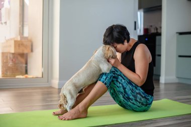 Esmer, orta yaşlı bir kadın evde köpekle egzersiz minderi üzerinde yoga yapıyor, akıl sağlığı, zihinsel denge, kendine zaman ayırıyor, stres atma, arabuluculuk, zihin dolgunluğu konsepti.