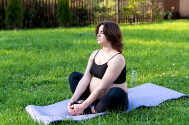 Hamile kadın dışarıda yoga yaparken nefes alıyor ve sakin, çimenler üzerinde esneme egzersizi yapıyor. Kendine Bakım, Yoga, Hamilelik, Doğum Konsepti. Anneliğin, sağlık hizmetinin, hobilerinin tadını çıkar..