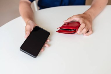 Evdeki masada oturan genç bir çocuk bir çanta ve akıllı bir telefonla mali sorumluluk öğreniyor ve birikimlerini öngörüyor. Finans kavramı, yatırım. İnternetten ya da genç müşterilerden para kazan