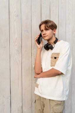 Kulaklık takan, telefonda konuşan, dışarıda konuşan, cep telefonu kullanan genç bir çocuk. Açık hava sohbetleri, akıllı telefondan konuşan bir genç..