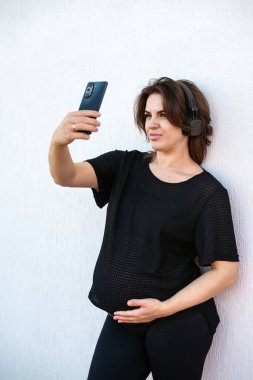 Hamile genç bir kadın cep telefonuyla selfie çekiyor ya da açık hava görüntülü görüşme yapıyor. Annelik, akıl sağlığı ve hamilelik kavramı.