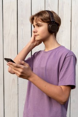 Kulaklıklı genç çocuk akıllı telefonlara bakıyor ve dışarıda sohbet ediyor, müzik dinliyor, konuşuyor ve telefonda daktilo ediyor, telefondan, çocuktan ve akıllı telefondan mesaj okuyor, sosyal medyayı kontrol ediyor..