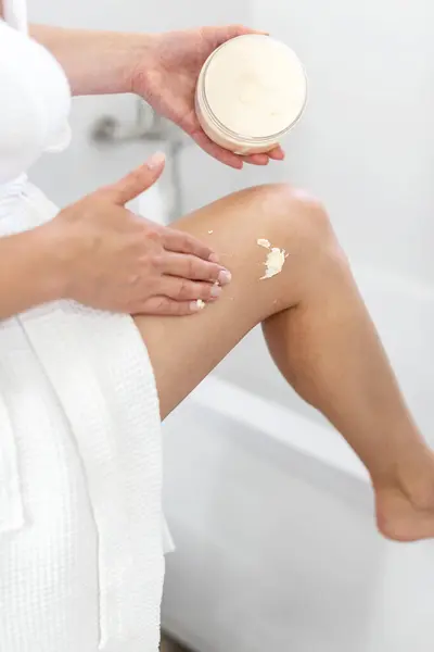 Beauty routine and body care. Cream, skincare and ethnic middle aged woman applied cosmetic moisturizing cream lotion on her body in bathroom. Beauty treatment at home