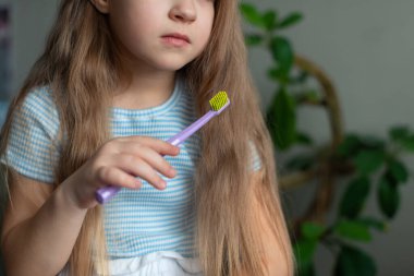 Mavi çizgili gömlekli, diş fırçası tutan beyaz bir kız..