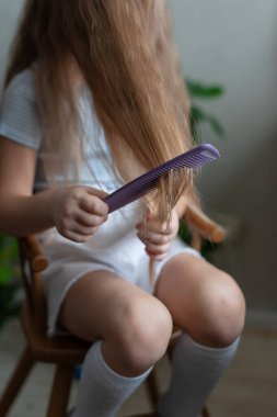 Genç beyaz kadın çocuk, rahat bir odada mor tarakla uzun saçlarını tarıyor..