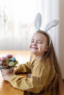 Paskalya sepeti içinde tavşan kulaklı, gülümseyen beyaz bir kız..