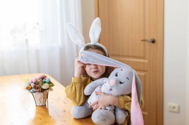 Tavşan kulaklı beyaz kız parlak odada sevimli oyuncaklarla oynuyor..