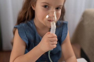 Evde solunum tedavisi için astım maskesi kullanan beyaz bir kız..