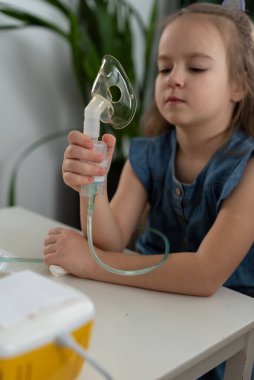Evde nebulizör kullanan beyaz bir kız çocuğu..