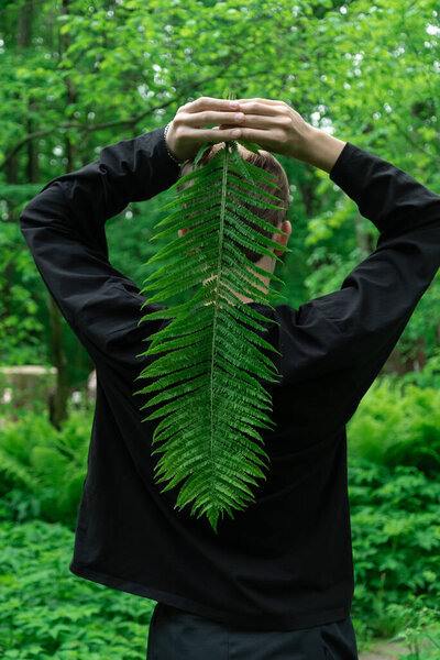 Кавказская молодая женщина держит лист папоротника в пышном зеленом лесу.