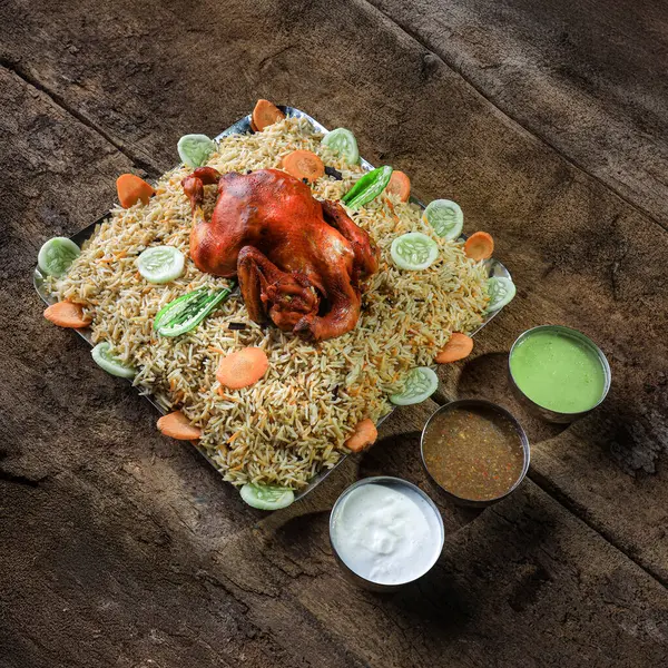Kızarmış tavuk, sebzelerle süslenmiş kokulu biryani pilavının üzerinde servis edilir. Geleneksel lezzeti arttırmak için yanında da baharatlı soslar. Kırsal ahşap bir masada zarif bir şekilde sunuldu..