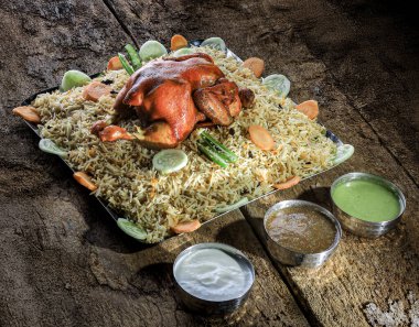 Çok güzel düzenlenmiş bir tabakta baharatlarla marine edilmiş taze sebzelerle süslenmiş lezzetli biryani pirincinin üzerinde dinlenen bir tavuk var. Mekan kırsal ve davetkar.