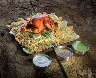 Çok güzel düzenlenmiş bir tabakta baharatlarla marine edilmiş taze sebzelerle süslenmiş lezzetli biryani pirincinin üzerinde dinlenen bir tavuk var. Mekan kırsal ve davetkar.