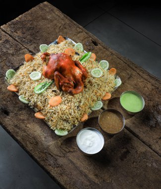 Çok güzel düzenlenmiş bir tabakta baharatlarla marine edilmiş taze sebzelerle süslenmiş lezzetli biryani pirincinin üzerinde dinlenen bir tavuk var. Mekan kırsal ve davetkar..