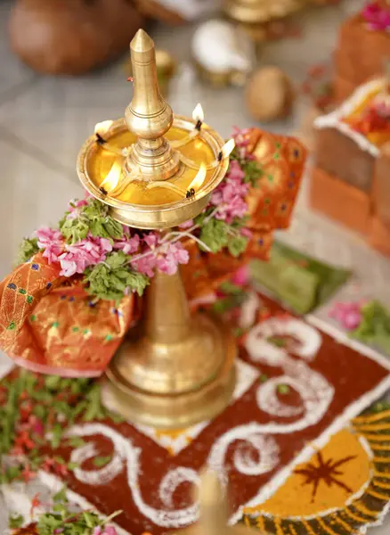 Kültürel ya da törensel bir kutlama sırasında, karışık rangoli desenlerinin yanına yerleştirilmiş, çiçek çelenkleriyle süslenmiş, birden fazla alevle aydınlatılmış, pirinçten bir gaz lambası..