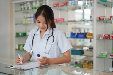 Medicine and health concept, Female pharmacist hold pill bottle and write prescription in pharmacy.