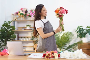 Çiçekçi konsepti, çiçekçi kadın dükkanda çiçek buketi yapmaya hazırlanmak için renkli gerbera tutuyor..