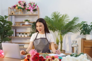 Çiçekçi konsepti, dizüstü bilgisayardan çiçek siparişlerini kontrol eden kadın çiçekçi ve mağazadaki not defterine not almak..