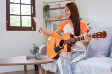 Guitar and singer concept, Young asian woman reading lyrics and playing music with acoustic guitar.