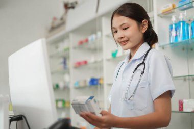 Medicine and health concept, Female pharmacist hold medicine product to working with cash register.