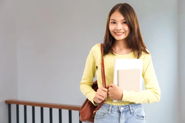 stock image Education and literacy concept, College student girl smile while carrying bag and holding textbook.